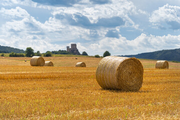 Fototapeta na wymiar Straw bales in the summer sun on a hillside in Hungary with a castle ruin in the background
