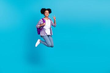 Full length photo of sweet shiny girl dressed checkered shirt jumping showing v-sign going college isolated blue color background