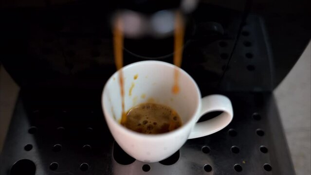 Coffee machine pouring arabica into a white espresso cup, slow motion, vertical screen
