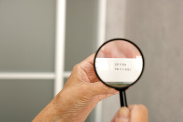 hands of an elderly man examining the expiration date of medicines with a magnifying glass