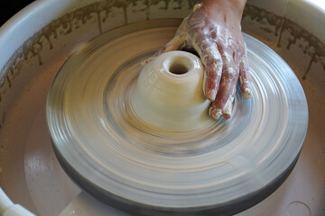 Craftsman's hands and potter's wheel. Close-up.