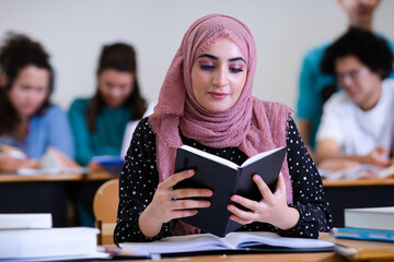 Beautiful Middle Eastern University College student at classroom with blurred classmates around. Arab Saudi, Qatar, UAE, Qatar, Oman, Bahrain, Kuwait education learning concept