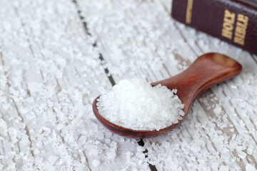 Salt in wooden spoon and holy bible book on table. Close-up. Christians are salt of the earth,...
