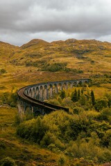 Fototapeta premium Scenic view of a train railway bridge over a lush landscape of mountains and grass