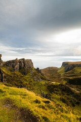 Picturesque mountain landscape featuring a rolling grassy hill dotted with rocks and a cliff