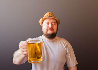 Portrait of young man wearing straw hat holding mug of beer. Selective focus on beer mug.