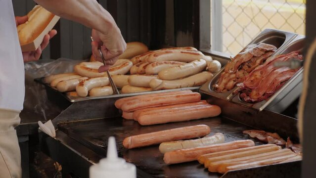 Cooking hot dogs in outdoor fast food restaurant, takeaway festival food truck. Sausages frankfurt and buns are fried and grill for delivery