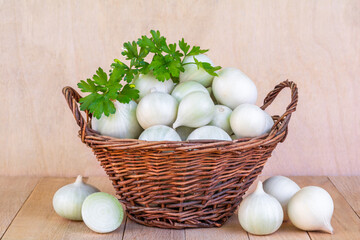 Ripe white onion bulbs in a wicker basket on a wooden table