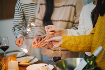 Cheerful friends enjoying home Birthday holiday party. Asian Friends hold lights with sparkling Sparkler celebrating Christmas or New Year eve party.