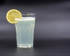 A glass of drink with a slice of lemon on a gray background