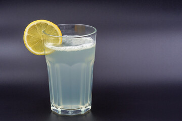 A glass of drink with a slice of lemon on a gray background