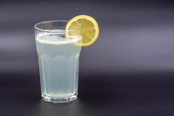A glass of drink with a slice of lemon on a gray background
