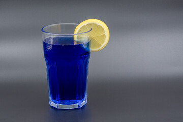 A glass of drink with a slice of lemon on a gray background