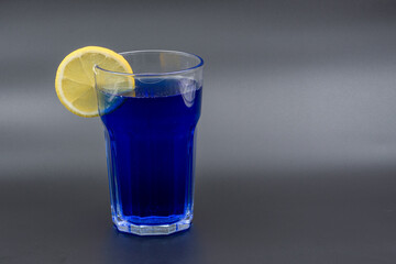 A glass of drink with a slice of lemon on a gray background