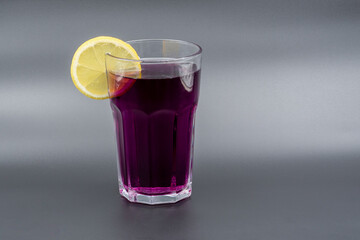 A glass of drink with a slice of lemon on a gray background