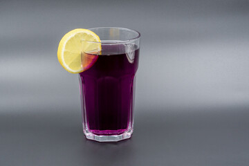 A glass of drink with a slice of lemon on a gray background