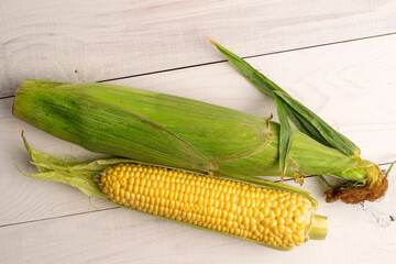 Two cobs of sweet organic corn, close-up, on a white wooden table, top view.