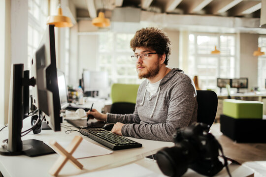 Young male photographer editing photos on his computer while working from the office