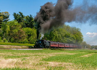 Obraz premium A View of an Antique Restored Steam Passenger Train, Approaching, Blowing Black Smoke, Traveling Thru Rural Countryside on a Sunny Day
