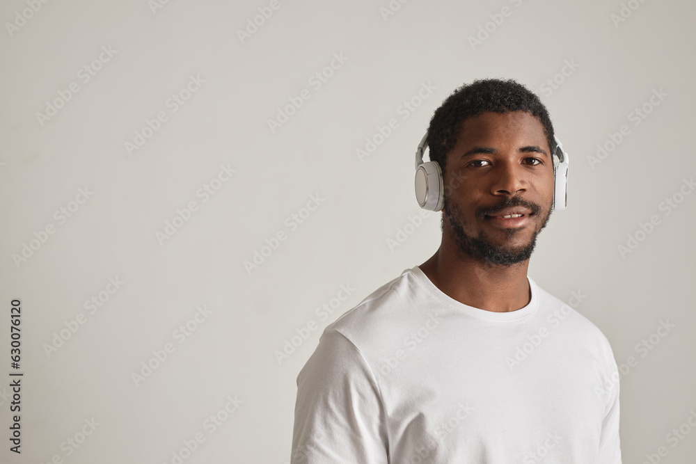 Wall mural Minimal front view portrait of black man wearing headphones against white background, copy space - Wall murals