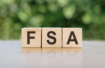 Letters of the alphabet of FSA on wooden cubes, green background. FSA - short for Flexible Spending...