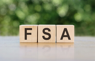 Letters of the alphabet of FSA on wooden cubes, green background. FSA - short for Flexible Spending Account