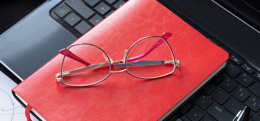 Office black workspace with office supplies. Red notebook with eyeglasses lie on laptop
