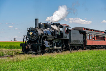 Fototapeta na wymiar A View of An Approaching Antique Restored Steam Passenger Train,, Blowing Smoke and Traveling Thru Farmlands on a Sunny Spring Day