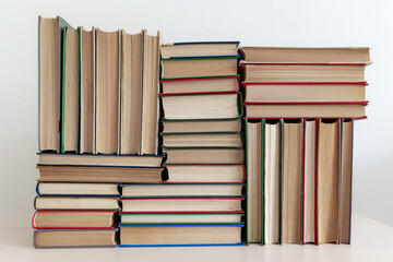 Stacks of thick old books in different bindings colors sizes lying and standing on light background