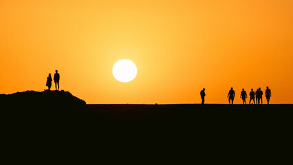 People silhouttes in desert watching big sun going down during epic sunset in Egypt.