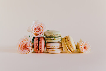 Tasty french macarons with tender rose flowers on a peach pastel background.