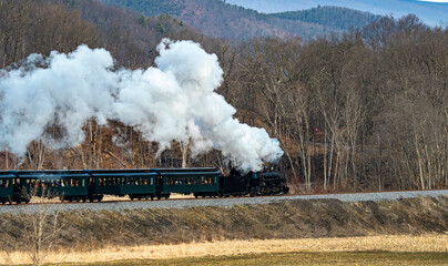 Fototapeta na wymiar View of a Narrow Gauge Restored Steam Passenger Train Blowing Smoke and Traveling Thru Farmlands on a Winter Day