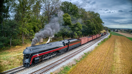 An Low Aerial View of a Streamlined Antique Steam Freight Train, Blowing Black Smoke and Steam Through Harvested Farm Lands, on a Fall Day