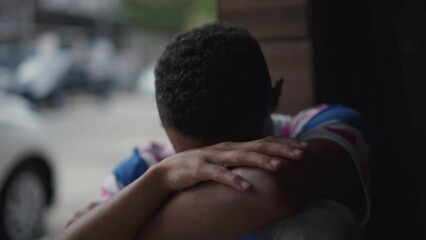 One depressed young black man struggles with social isolation and mental illness, covering face in shame and regret. Person of African American descent facing quiet despair