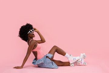 Happy black woman with roller skates on pastel pink background.