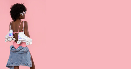 Happy black woman with roller skates on pastel pink background.