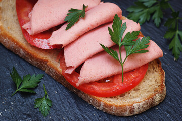 Cold sandwich with sliced mortadella in italian style. Closeup view on cooked meal with rye bread and tomatoes. - 630083533