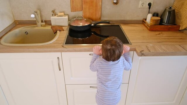 Baby climbs on a hot electric stove in the home kitchen. A small child touches the surface of the stove with his hand at the risk of getting burned. Kid aged about two years (one year nine months)