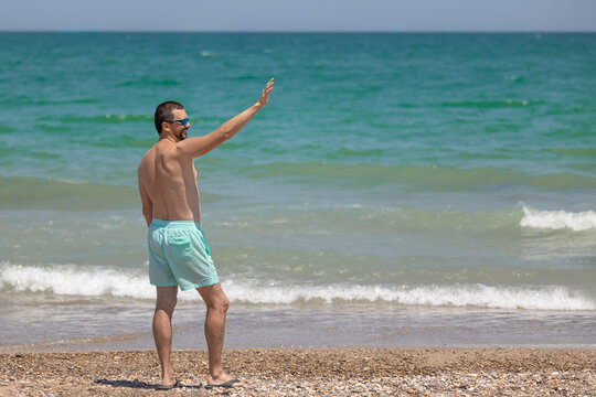 A young white man in sunglasses with a beard waves his hand.