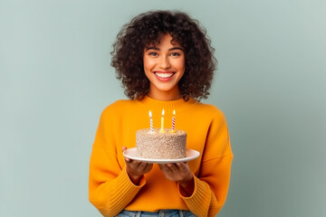 Happy  young woman in warm sweater smiling and holding birthday cake with candle  