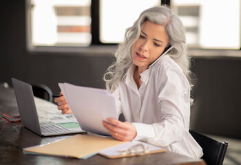 Middle Aged Businesswoman Talking On Phone Holding Papers In Office