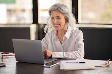 Middle Aged Businesswoman Looking At Laptop Computer Smiling At Workplace