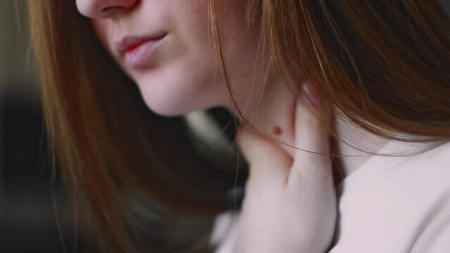 Close-up of a young woman, sick, holding her sore throat with her hands. A sore throat