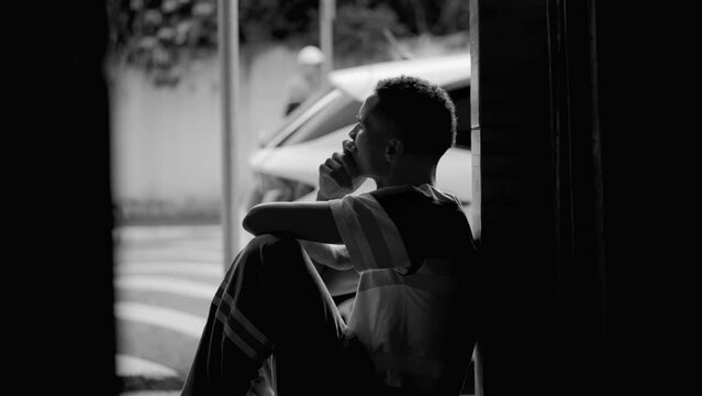 Thoughtful person from African American descent observing neighborhood from door front gazing with pensive contemplative expression, dramatic black and white