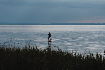 Fototapeta na wymiar young man standing on sup and paddling on water of calm lake, tranquil scenery
