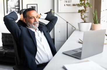 Naklejka premium Glad positive caucasian senior businessman in suit resting, looking at computer in modern office