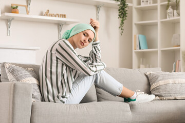 Teenage girl after chemotherapy sitting on sofa at home