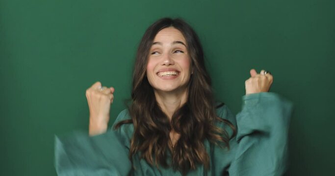 Woman gesticulating waiting for special moment say please yes winner isolated on green background in studio. Girl crossing fingers, looking up and begging please. Screaming yes, girl winning.