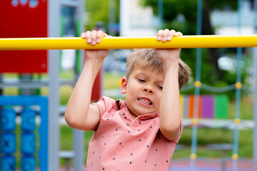 Boy playing sports on street sports ground. Boy pulling himself up on horizontal bar..