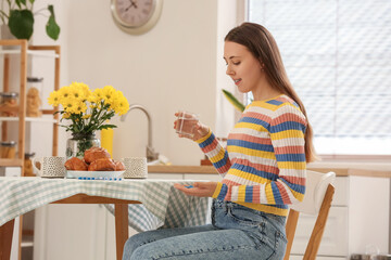 Young pregnant woman with glass of water taking Folic Acid pills in kitchen